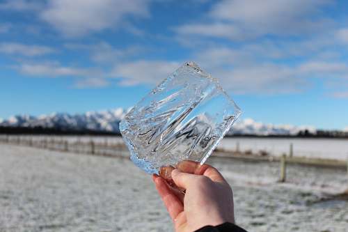winter person holding clear shard under blue sky snow